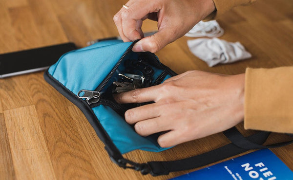A person placing keys in the front zippered pocket of the P.I.K.A. Pouch.